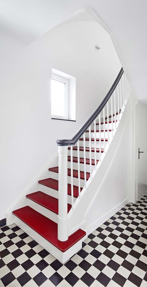 Modernisiertes Treppenhaus mit roten Stufen und Schachbrettmuster-Fliesenboden.