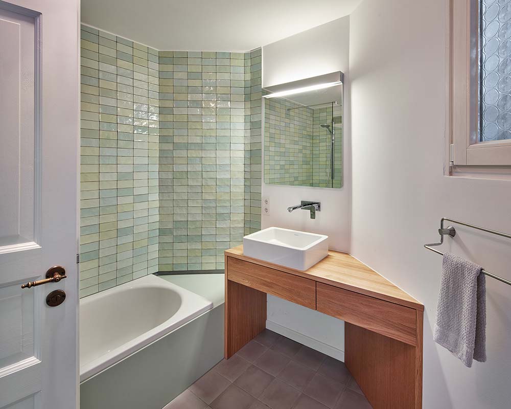 Modernes Badezimmer mit Holzwaschtisch und hellgrünen Kacheln.