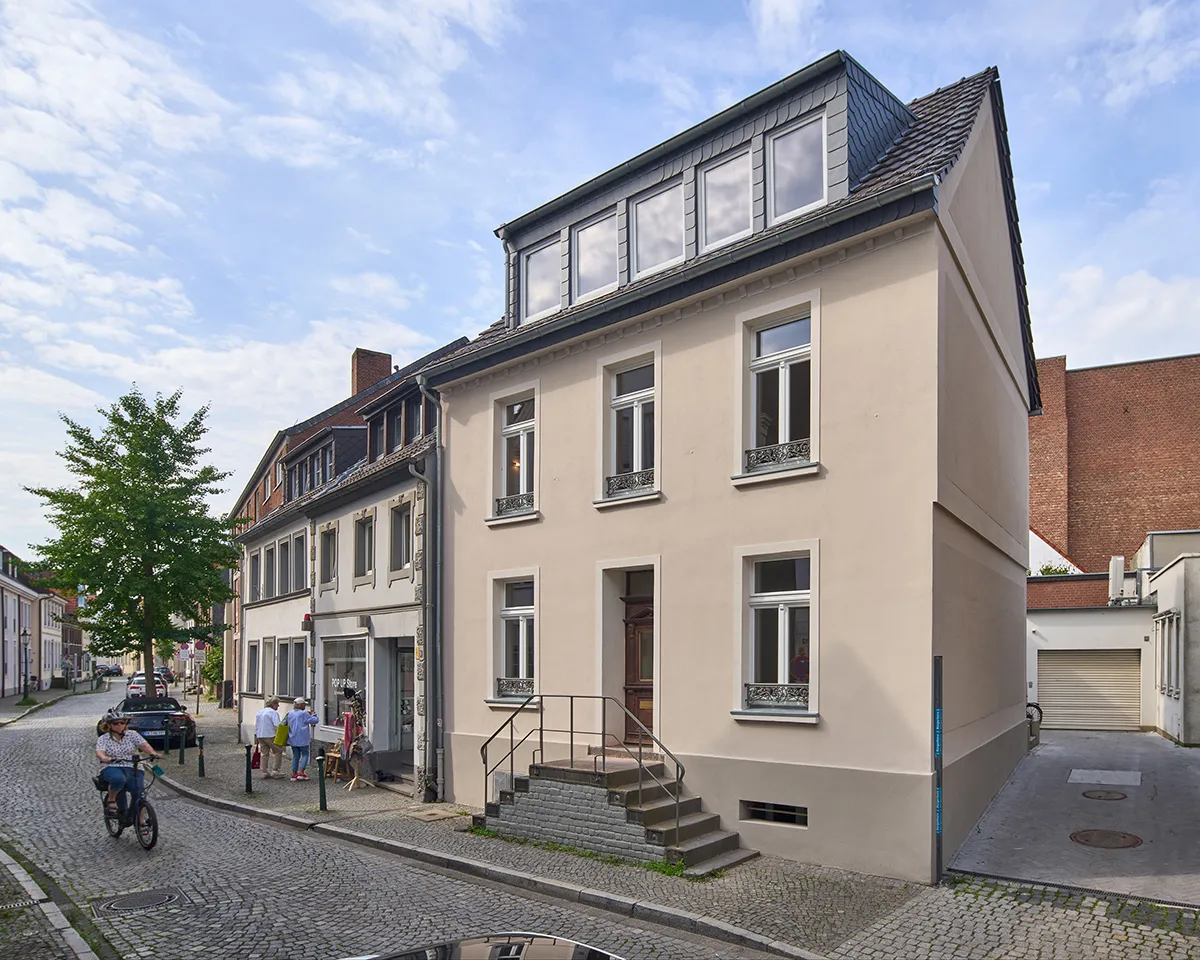 Saniertes Stadthaus mit heller Putzfassade, neuen Fenstern und ausgebautem Dachgeschoss in historischer Straßenzeile.