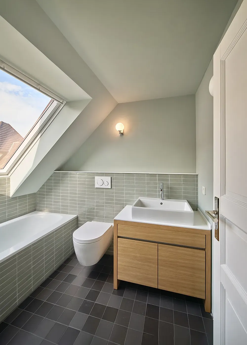 Saniertes Badezimmer im Dachgeschoss mit Badewanne, wandhängendem WC, Waschtisch und Dachflächenfenster.