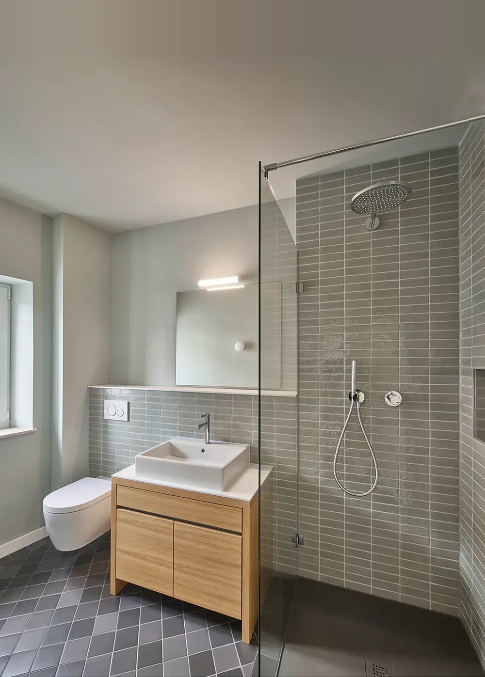 Saniertes Badezimmer mit bodengleicher Dusche, Waschtisch, wandhängendem WC und großformatigem Spiegel.