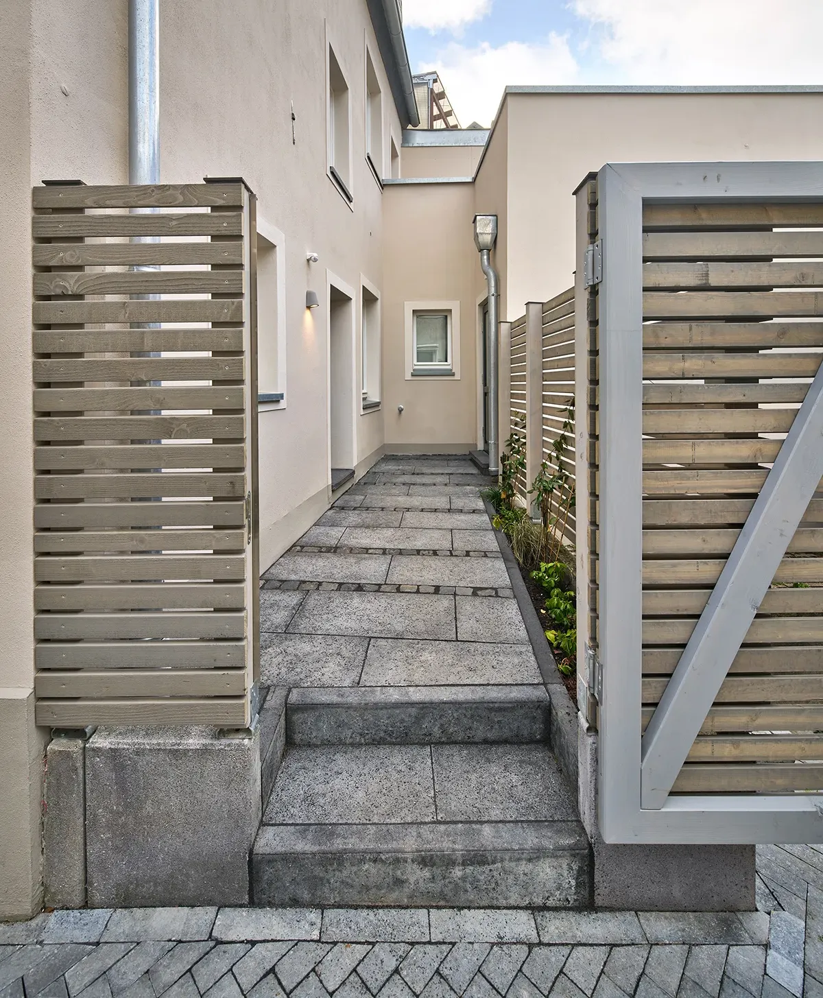 Wohnbereich einer Maisonettewohnung mit großer Fensterfront, moderner Ecksofa-Lösung, farbigem Teppich und Zugang zur überdachten Terrasse.