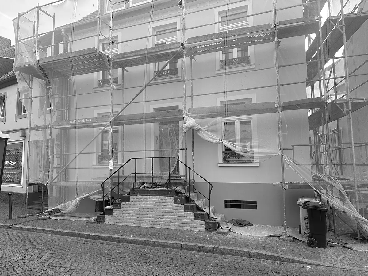 Straßenansicht des Stadthauses während der Sanierung mit Fassadengerüst, Schutznetzen und freigelegtem Eingangsbereich.